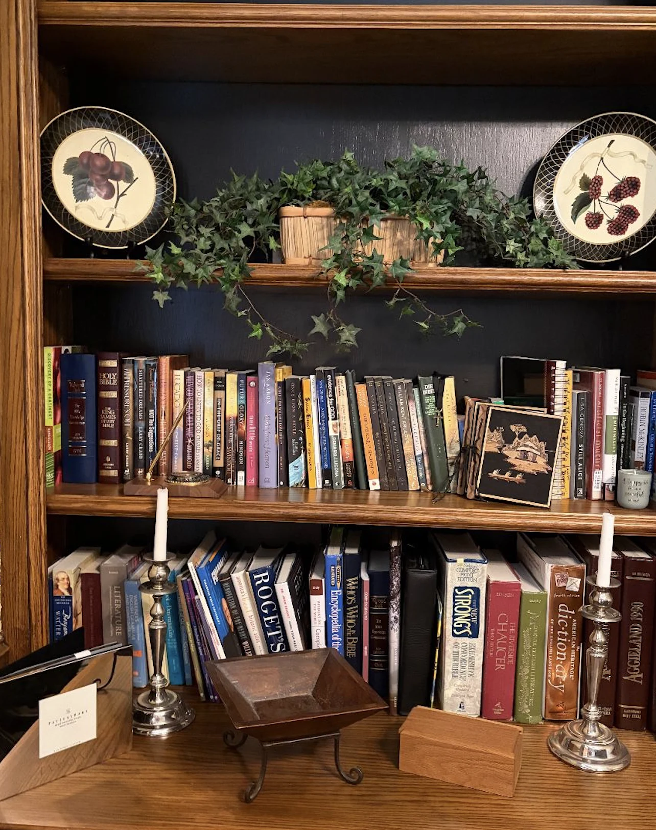 Books, decorative plates, and greenery arranged in a wooden bookcase at a Spring estate sale